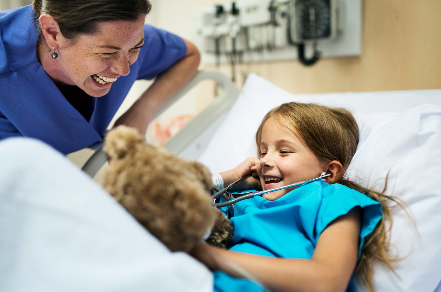 Ein Mädchen lacht im Krankenhausbett mit einer Pflegerin
